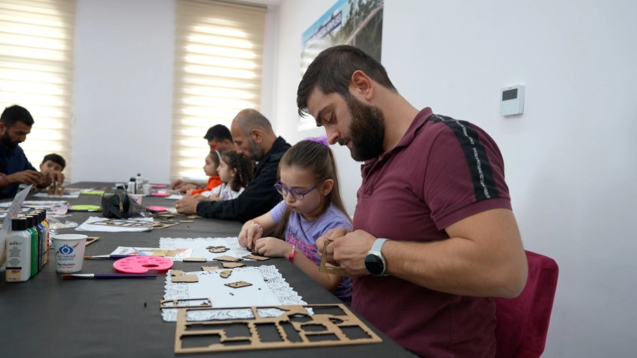 Kızıyla birlikte maketle uğraşan baba ve arkada blurlu bir şekilde kendi maketleriyle uğraşan diğer insanlar