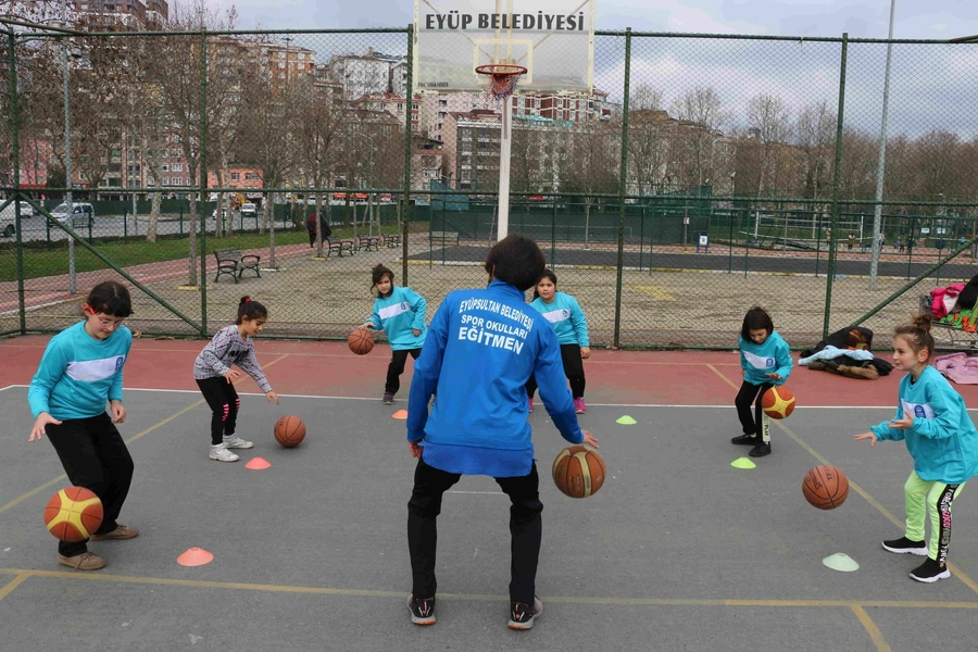 Eğitmenle birlikte basket sahasında top sektiren çocuklar